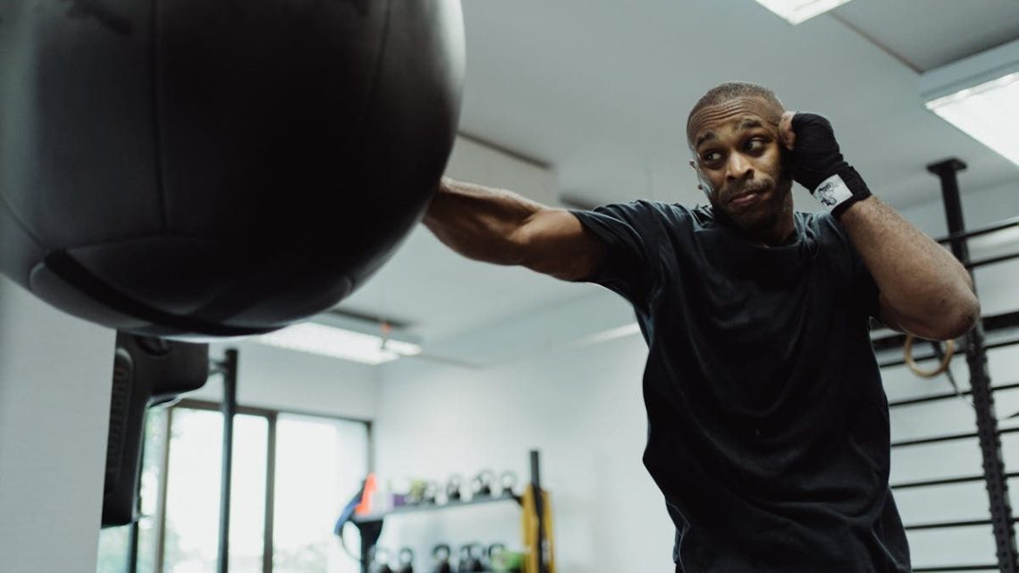 Boxer in black shirt intensely punching a heavy bag during training indoors.