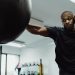 Boxer in black shirt intensely punching a heavy bag during training indoors.